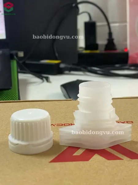 Vòi nhựa trắng và nắp vặn trắng dùng gắn lên túi có vòi, đặt trên bàn mẫu