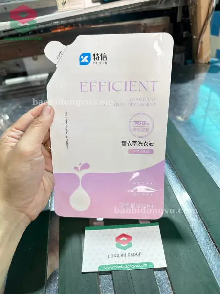 Túi có vòi in nền trắng hồng, vòi góc xéo, cầm trên tay cạnh danh thiếp Đông Vũ tại xưởng