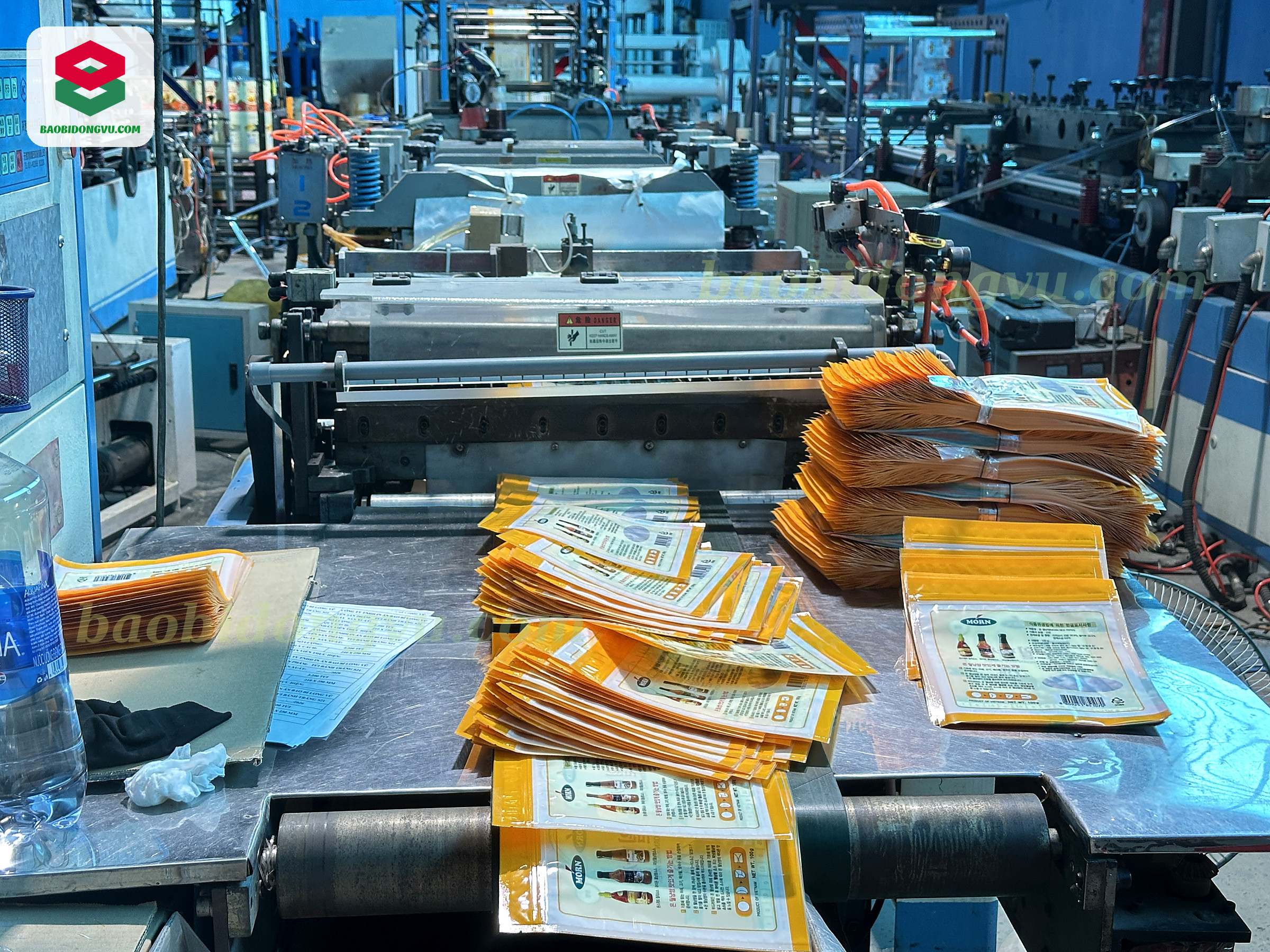 Stacks of finished custom printed pouches at the bag-making machine outfeed, Dong Vu Packaging factory in Ho Chi Minh City